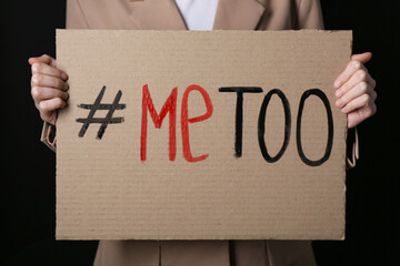 Woman holding cardboard paper with hashtag METOO on dark background, closeup