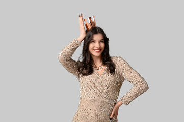 Beautiful young woman in stylish prom dress and paper crown on grey background