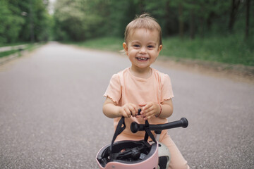 Smiling toddler girl posing on push scooter with safety helmet
