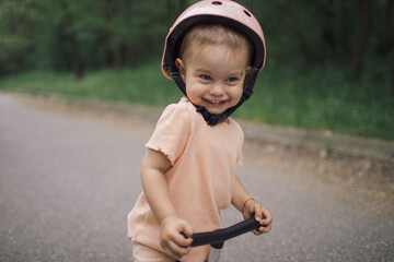 Toddler girl posing on push scooter wearing safety helmet