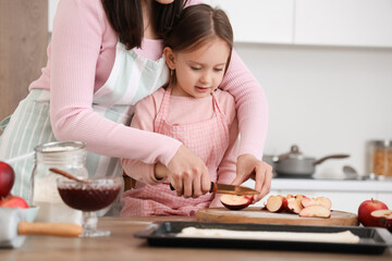 Cute little girl with her mother cutting apple in kitchen on holiday