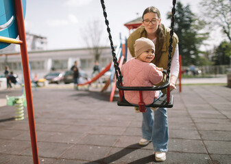 Mother posing with daughter on playground's swing