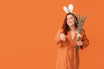 Beautiful young woman in bunny ears with pussy willow branches on orange background. Easter...