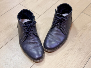 Old and dirty black lace-up shoes are on the ceramic tiles in the hallway of the house