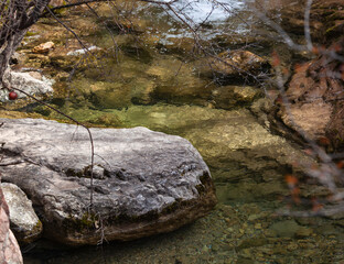 The stone lies in the riverbed, amidst a natural landscape of grass and wood. A mountain river. A...