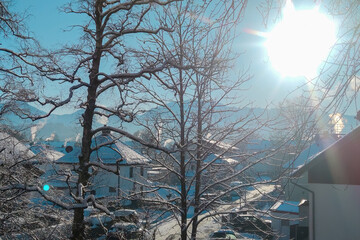 Winter landscape in a town, with the Alps mountains in the background. Trees in hoarfrost against a beautiful morning sky on a frosty morning. Snow cannons spread snow on the slopes