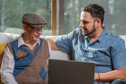Adult and happy older father next to his adult son having a relaxed conversation enjoying the moment together in the comfort of their home. Two generations father and son.