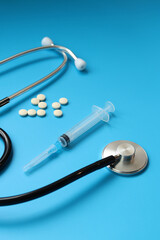 Stethoscope, pills and syringe on blue background, selective focus. Cardiology and healthcare concept. Auscultation device. Medical care concept. Medical instrument. Auscultation apparatus