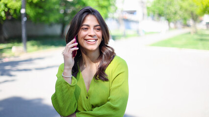 Beautiful, young Latin American woman walking down the street and talking on mobile phone