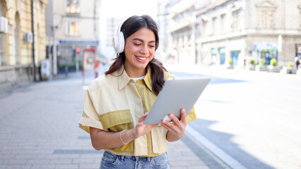 Beautiful, young Latin American woman with headphones using tablet on the street