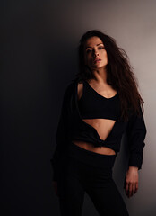 Sexy young beautiful woman posing in black fashion sporty top, shirt and trousers on studio wall background. Closeup