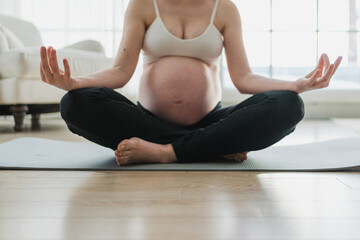 Pregnancy prenatal breathing. Pregnant woman with big belly sitting in lotus pose on yoga matt at...