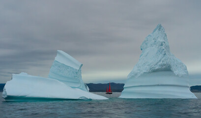 two icebergs with red sailboat in Greenland
