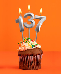Birthday cupcake with number 137 candle - Orange color background