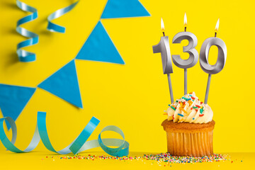 Lighted birthday candle number 130 - Yellow background with blue pennants