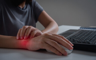 Young woman working in an office with carpal tunnel syndrome or wrist joint inflammation, massage...