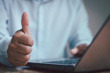 Successful businessman showing thumb up at workplace with a laptop computer. Recommended with thumbs up, accept, good, best or great choice, indicating approval or showing that one likes something.