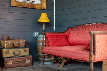 The interior of a vintage living room with a colorful red velvet couch, stack of antique leather...