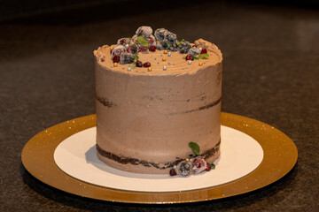 A chocolate whipped frosted cake with maceration berries.The delicious sweet is decorated with blueberries, pomegranate, and cranberry sugared crystal fruit. The whipped dessert has mint leaves on top