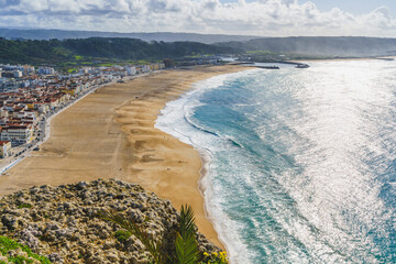 Expansive view of Nazare beach and town from a high vantage point with the sun glistening on the water.