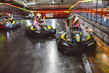 Friends competing in Go kart racer hit each other's cars in an accident while raising their hands in anger. Indoor kart track - obrazy, fototapety, plakaty