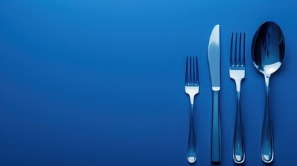 Silver cutlery set including knife, fork, spoon, and teaspoon on blue background - obrazy, fototapety, plakaty