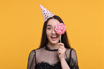 Happy woman in party hat holding lollipop on orange background - Powered by Adobe