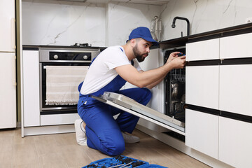 Serviceman repairing dishwasher with screwdriver in kitchen