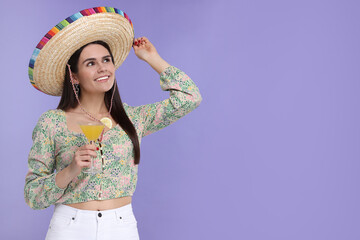 Young woman in Mexican sombrero hat with cocktail on violet background. Space for text