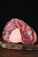 Piece of raw beef meat on wooden table against black background, closeup