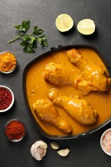 Tasty chicken curry and ingredients on black textured table, flat lay
