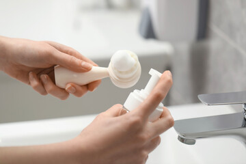 Washing face. Woman applying cleansing foam onto brush above sink in bathroom, closeup