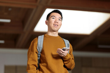 A student in the school foyer holding a phone with a smile