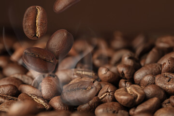 Roasted coffee beans falling on heap against brown background, closeup