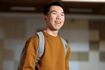 A young student in a brown sweater and backpack happily standing in a classroom