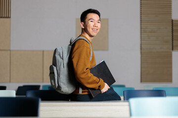 An Asian student sitting on the desk in the middle of the classroom