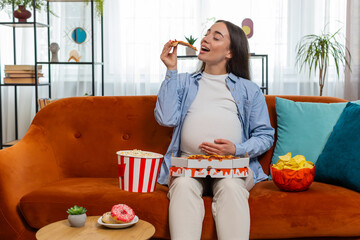 Pregnant woman girl eating unhealthy junk food pizza, popcorn crisp sitting on couch watching TV...