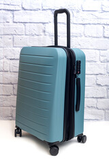 suitcase on wheels stands against a brick wall.