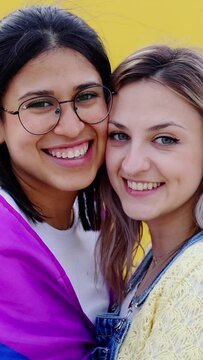 Vertical portrait of lovely young lesbian couple hugging each other smiling at camera over yellow background. LGBTQ and love concept