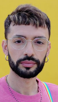 Close-up vertical portrait of young cheerful bearded gay man looking at camera over yellow background. LGTBQ people concept