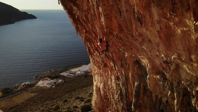 Climber climbing a hard and steep section of Grande Grotta cave at sunset and with Telendos island and coastline in the back at Kalymnos island, Greece. High quality 4k footage.