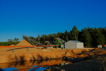 Industrial equipment for sand mining. Equipment for extracting sand is situated on the shore of a pond , surrounded by a pine forest. Sand quarry. - 786743078