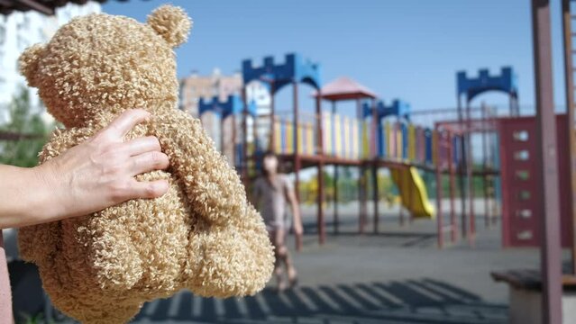 Person luring with teddy. A view of playground with person luring the child with teddy bear in hands in the sun light.