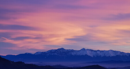 Tramonto luminoso viola arancio e rosa sopra le montagne innevate