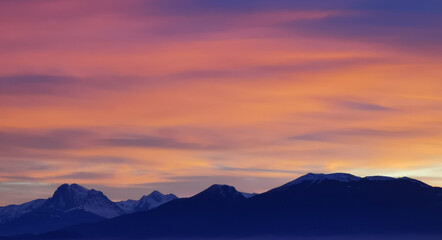 Obraz premium Tramonto luminoso viola arancio e rosa sopra le montagne innevate