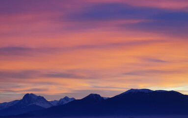 Tramonto luminoso viola arancio e rosa sopra le montagne innevate