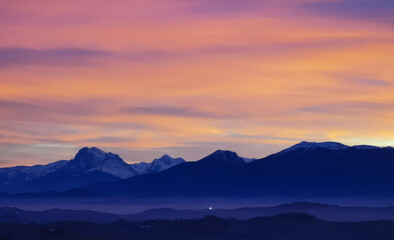 Tramonto luminoso viola arancio e rosa sopra le montagne innevate