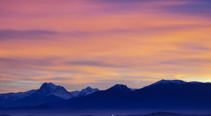 Tramonto luminoso viola arancio e rosa sopra le montagne innevate