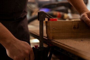 Carpenter using bench vise to hold timber block, starting furniture assembling in workshop, close...
