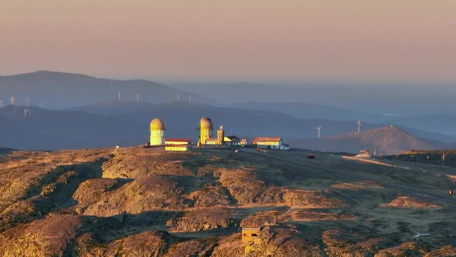 Telephoto aerial sunrise view of old abandoned radar station with wind turbines in background on top of Serra da Estrela Nature Park, Portugal
